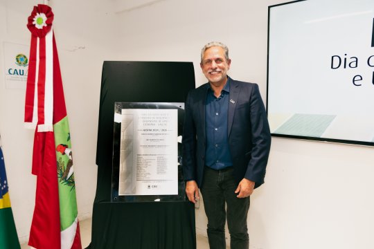 Presidente Carlos Alberto Barbosa de Souza ao lado de placa de lançamento da obra da Sede do CAU/SC em noite de premiações e lançamento da obra. 